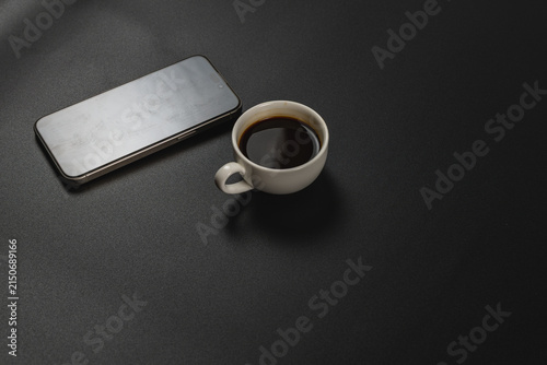 Smartphone beside a cup of coffee on a dark desk at a workspace