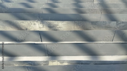 Close-up abstract background of grey metal roof tile layers with light and shadow play.