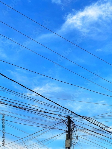Disorganized overhead power line infrastructure with high voltage transformers under a cloudy sky.