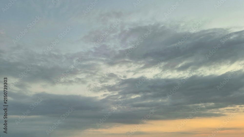 Obraz premium Dramatic Grey Clouds Stretching Across a Calm Sunset Sky at the Golden Horizon