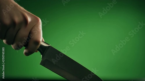 A hand holding a sharp chef's knife against a green background.
