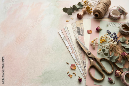 Scrapbook materials, decorative paper, dried flowers and scissors arranged on a soft pastel background for handmade projects. Paper crafts, memory keeping and creative hobby concept. Copy space