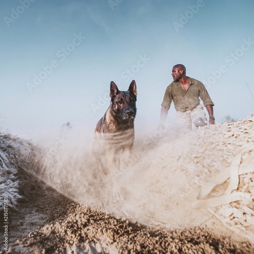 Working dog and Black veteran handler with a prosthetic leg training on a dusty obstacle course for rehabilitation and Veterans Day campaigns