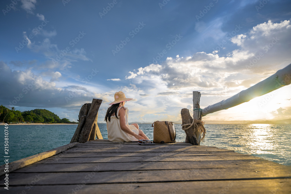 Fototapeta premium Woman tourist in moment easy going and relax on wooden pier, enjoy sunset of the summer trip in Koh Thalu island locate in Prachaup province,THAILAND