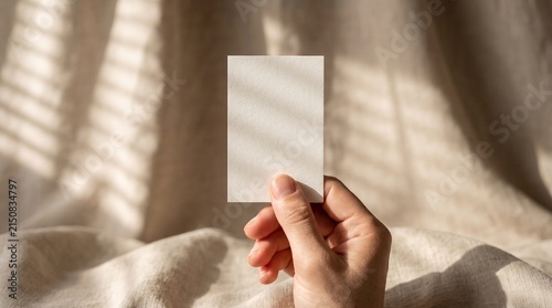 Hand holding a blank white card mockup against a soft textured fabric background