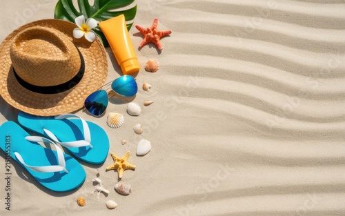 Summer beach vacation accessories including straw hat, blue flip flops, sunscreen bottle, and seashells arranged on textured sand with tropical palm leaf and plumeria flower