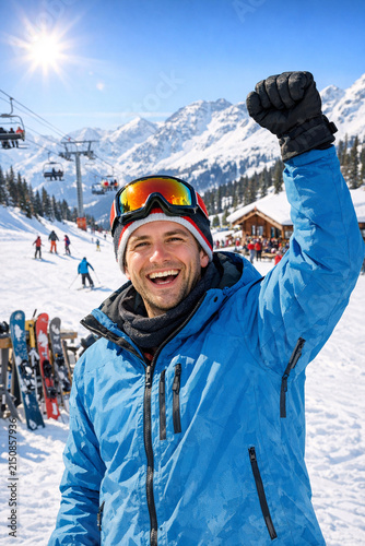 A man celebrating a skiing victory on the mountain top. He is wearing goggles and holding up a fist while standing in front of a ski lift.