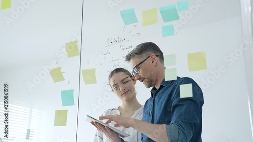 Colleagues collaborating on a clear glass board, brainstorming business strategy, developing innovative ideas, and organizing project tasks with colorful sticky notes in a modern office