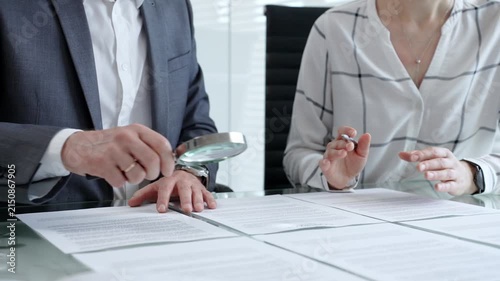 Business professionals reviewing legal contracts and important documents with a magnifying glass, performing careful examination and due diligence for risk assessment