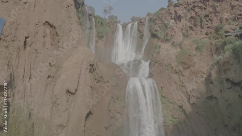 Dynamic handheld panning shot cutting across majestic Ouzoud Waterfalls and rainbow arc