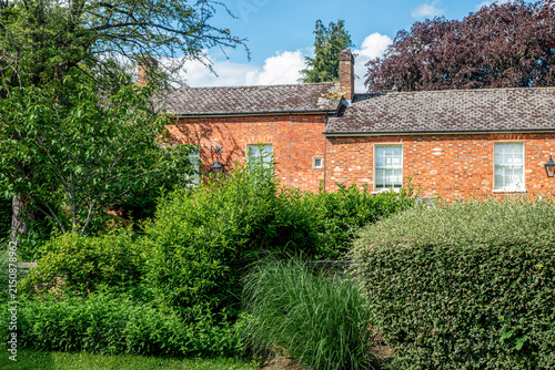 Traditional red brick house surrounded by lush garden greenery in the English countryside on a sunny summer day.