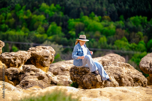 Woman resting on mountain rock in green forest valley. Peaceful summer outdoor recreation and calm travel adventure concept