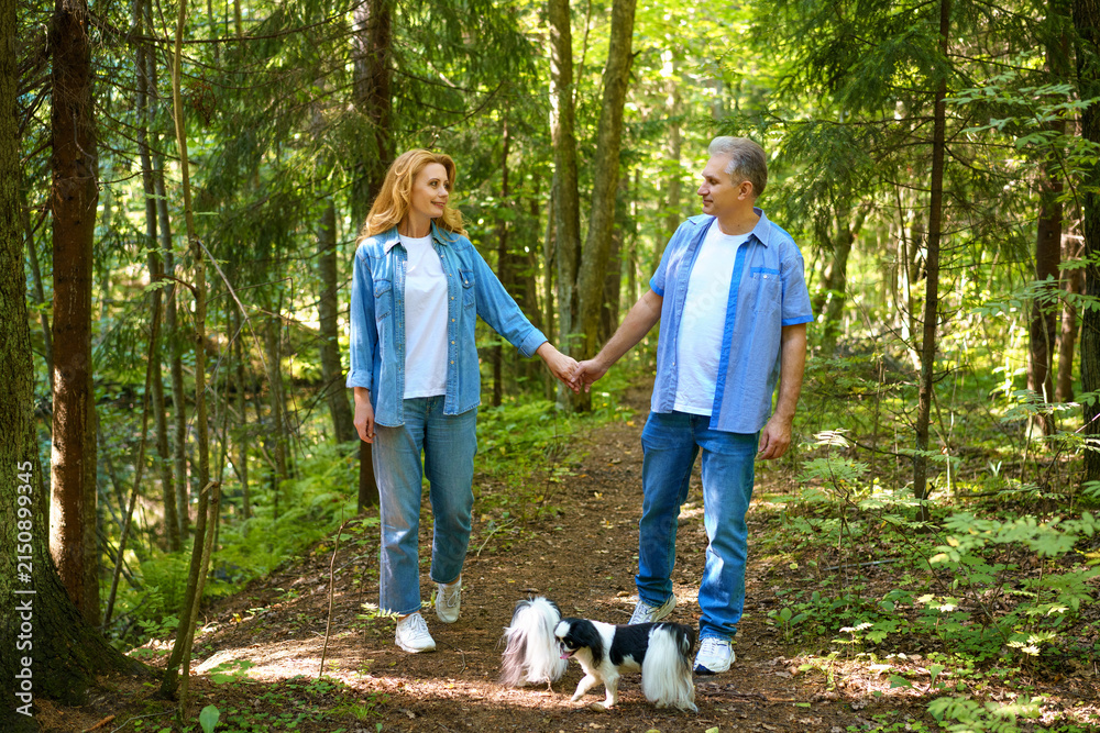 Fototapeta premium Mature Couple Walking Two Small Dogs on a Forest Path