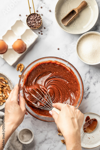 Process of making chocolate brownie. Female hands whisk the dough in glass bowl, top view. Home baking culinary concept, recipe