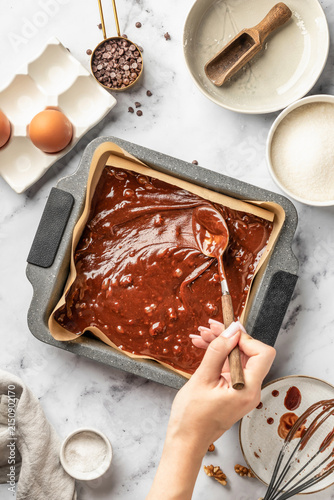 Process of making chocolate brownie. Female hands spread the dough in a baking pan, top view. Home baking culinary concept, recipe