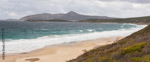 Coastal beach scene featuring a sandy shoreline, rocky headland and gentle ocean waves under cloudy natural light. A clean coastal landscape suitable for travel, nature, tourism and outdoor enviro