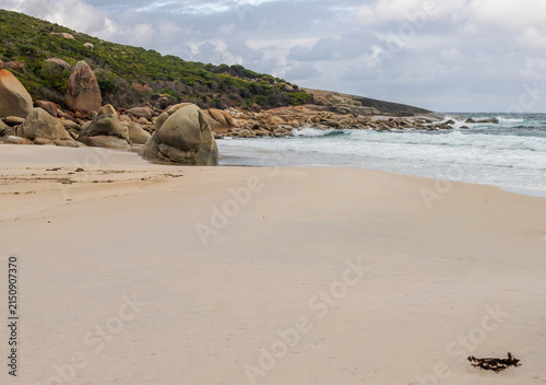 Coastal beach scene featuring a sandy shoreline, rocky headland and gentle ocean waves under cloudy natural light. A clean coastal landscape suitable for travel, nature, tourism and outdoor enviro