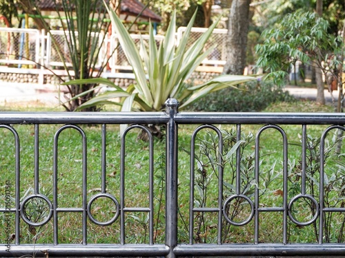 Decorative stainless steel fence railing along a green grass lawn in a public park setting.