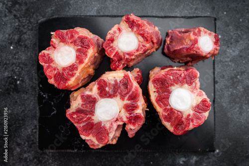 Cuadro en lienzo Beef oxtail sections ready for cooking on black plate, overhead composition on d