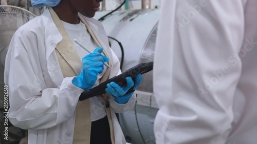 Closeup woman engineer using tablet recording data while man colleague checking juice bottling machinery factory plant, Industrial food beverage manufacturing team.