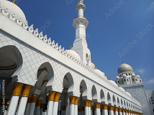 Photography mosque arcade corridor with gold detailed pillars minaret and dome under blue sk