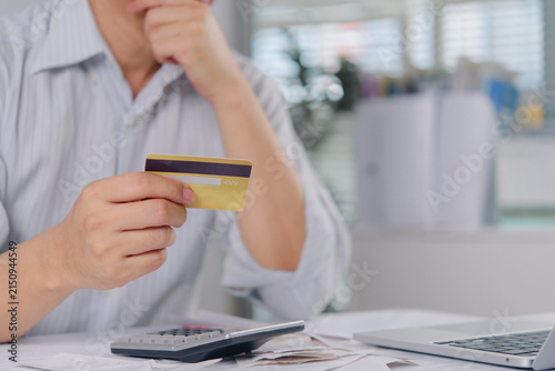 Man holding credit card and thinking about debt with calculator and receipts on desk