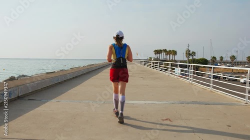 Woman runs along a coastal pier. Keyframes capture her progression from start to ocean. She wears red shorts and a blue vest. Her determined look shows focus. Ideal for health and wellness projects