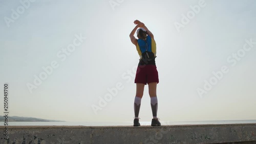 Person stretches on a concrete pier at sunset. Sunlight glints off the calm sea. They hold a board and wear sportswear. Their expression shows focus and readiness. Ideal for fitness, wellness
