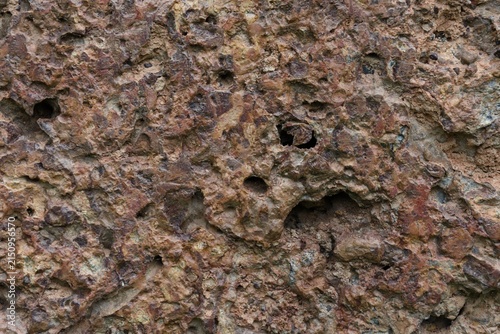 фотографія stone wall with pitted porous surface and reddish brown tone.