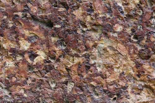 фотографія stone wall with pitted porous surface and reddish brown tone.