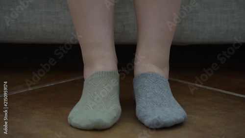 Close-up of woman's hands putting on mismatched socks of different color on her feet. Woman wearing different colored socks. Uniqueness, difference and independence concept. Front view