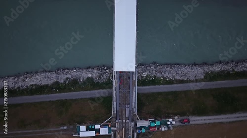 Top-down drone footage showing a railway bridge construction site with a temporary white protective roof and the interrupted railway line on both sides of the river crossing.