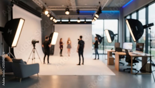 out of focus view of modern professional photography and video production studio with softbox lights, white backdrop, and creative team.