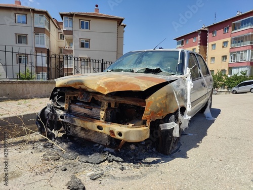 Photography Burned and severely damaged passenger car parked on a suburban street, representing tragic accident, total financial loss, unexpected vulnerability, urban crisis, and the fragility of security