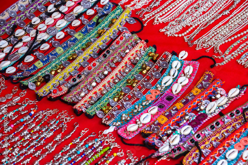 Fotografie Assorted colorful handmade Indian bracelets and anklets decorated with cowrie shells, bells and embroidery on display at a market in Hampi, India