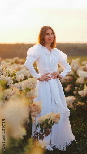 Fotografía Woman in white vintage dress standing in a field of flowers at sunset
