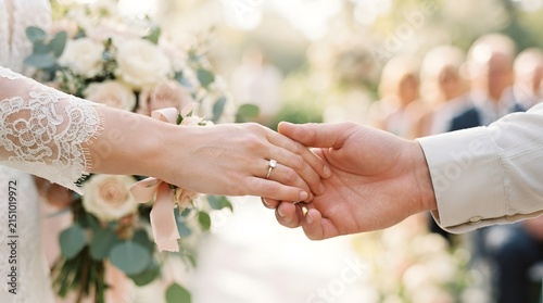 Bride and groom holding hands at wedding ceremony with bouquet and engagement ring