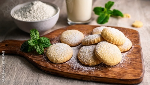 deliciously simple homemade shortbread cookies lightly dusted with powdered sugar and garnished with fresh mint served on wooden board with ingredients like flour and milk nearby creating inviting