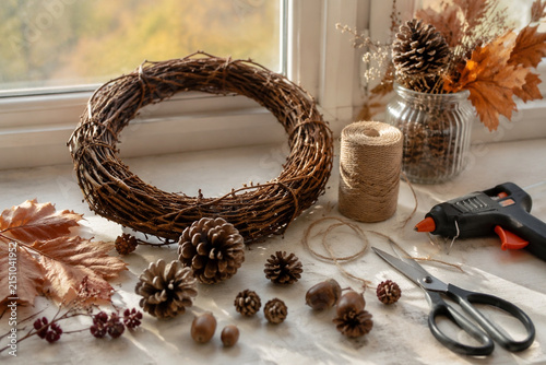 Window ledge still life with grapevine wreath, pinecones, acorns, jute twine, scissors and glue gun, autumn craft and DIY decor concept.
