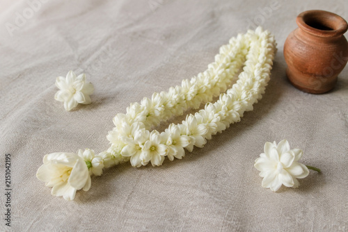 Sampaguita garland on linen with terracotta vase and jasmine blossoms, calm and safe decor concept