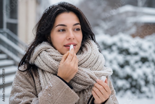 Young woman applying lip balm in a snowy winter day