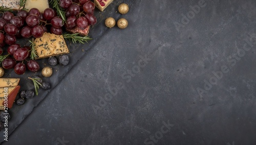 A delicious cheese and fruit platter with grapes, blueberries, and rosemary on a dark slate background, ready to be enjoyed