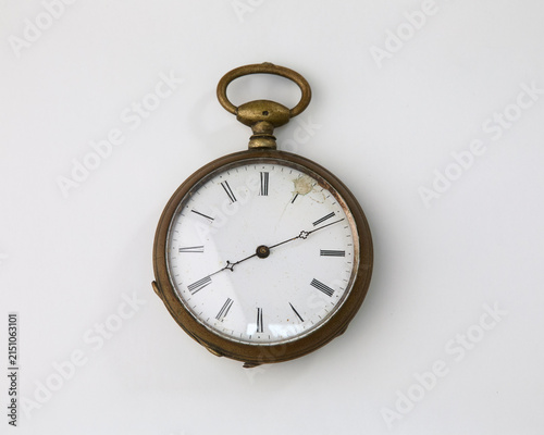 Vintage brass pocket watch with a simple white dial and black line markers, resting on a clean white background. A classic and historical timepiece.