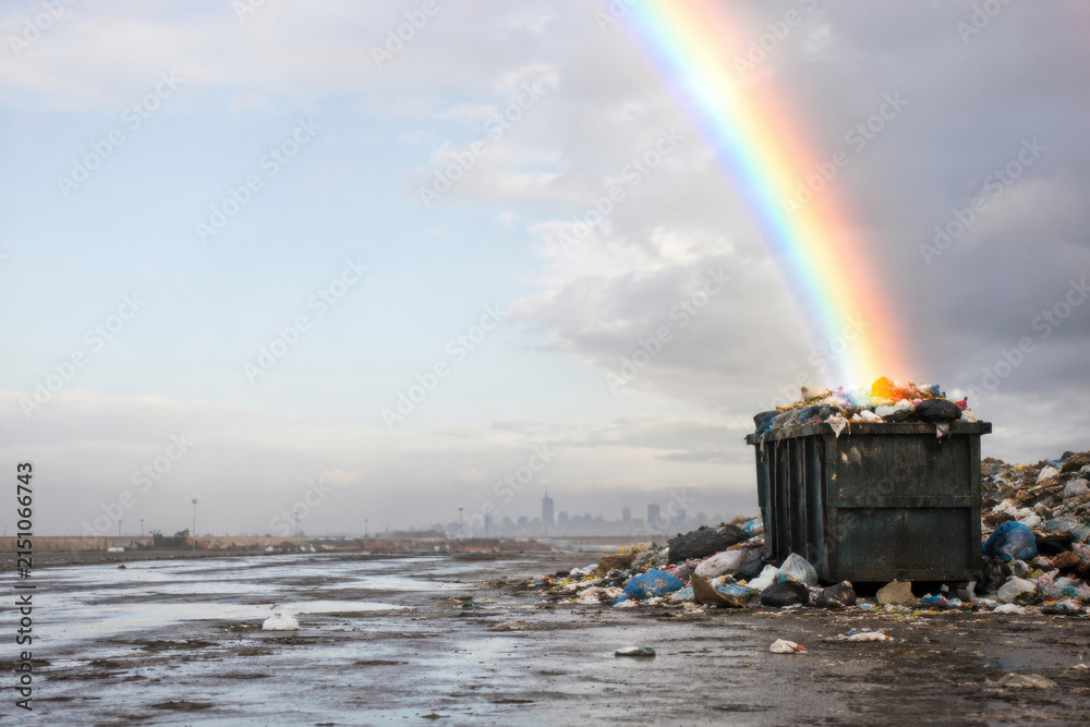 Fototapeta premium Rainbow ends above an overflowing garbage dumpster. Space for text.