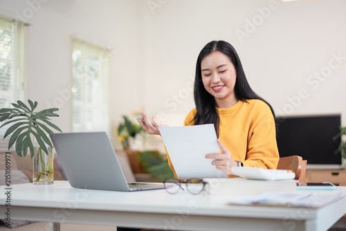Asian woman reviewing documents while working from home on a laptop