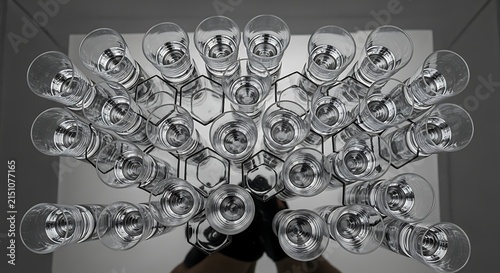Top down view of an array of clear glass tumblers arranged in a geometric honeycomb pattern reflecting light in a modern minimalist studio setting