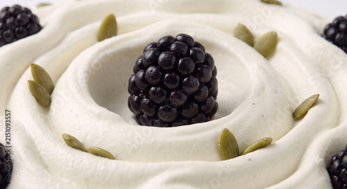 Distant shot of 5 to 10 blackberries and pumpkin seeds nestled on thick white vanilla Greek yogurt