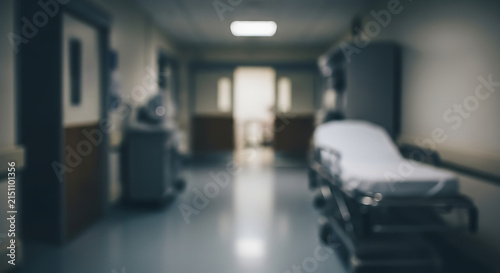 Hospital bed stands in a blurred medical corridor setting that suggests a professional care environment.