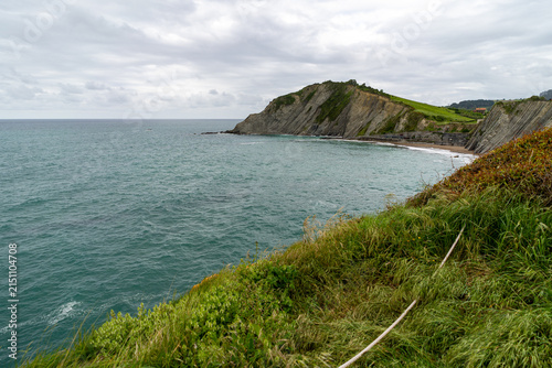 A scenic view of the rugged coastline and choppy ocean waters near Zarautz, Spain, under a cloudy sky