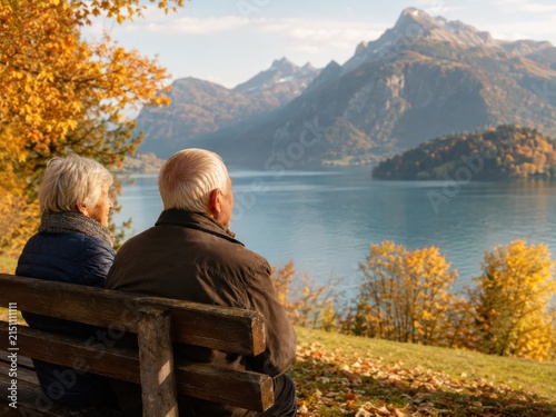 Seniorenpaar auf einer Bank mit Blick auf einen herbstlichen See in der Schweiz. Die friedliche Szene verbindet Naturgenuss, Reisen im Alter und die Ruhe eines goldenen Herbsttags.